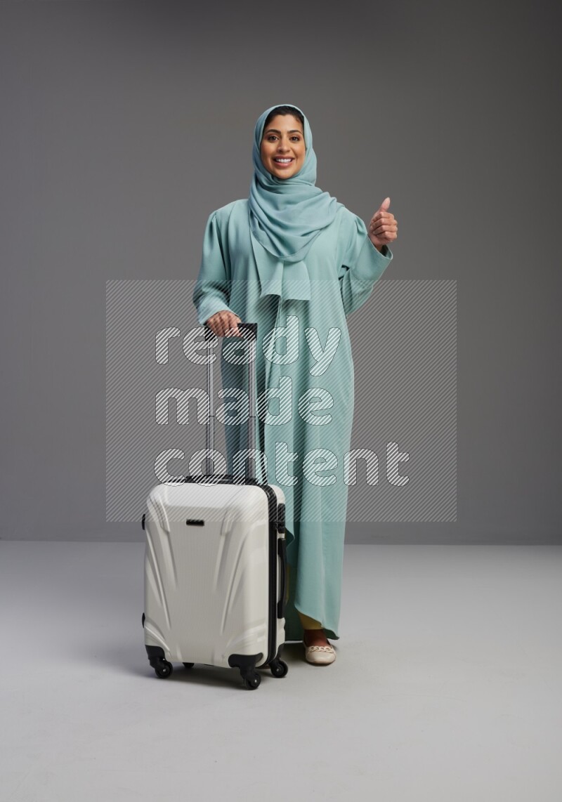 Saudi Woman wearing Abaya standing holding Travel bag on Gray background