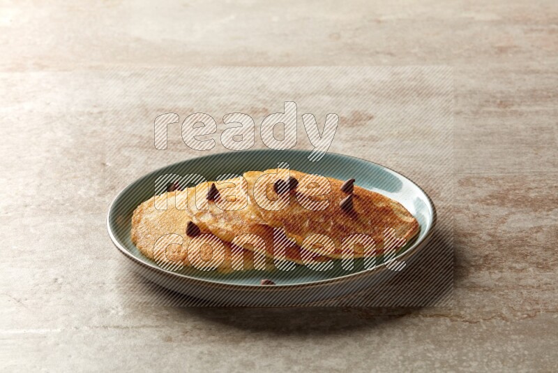 Three stacked chocolate chips pancakes in a blue plate on beige background