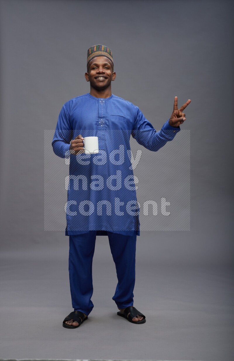 Man wearing Nigerian outfit standing holding mug on gray background