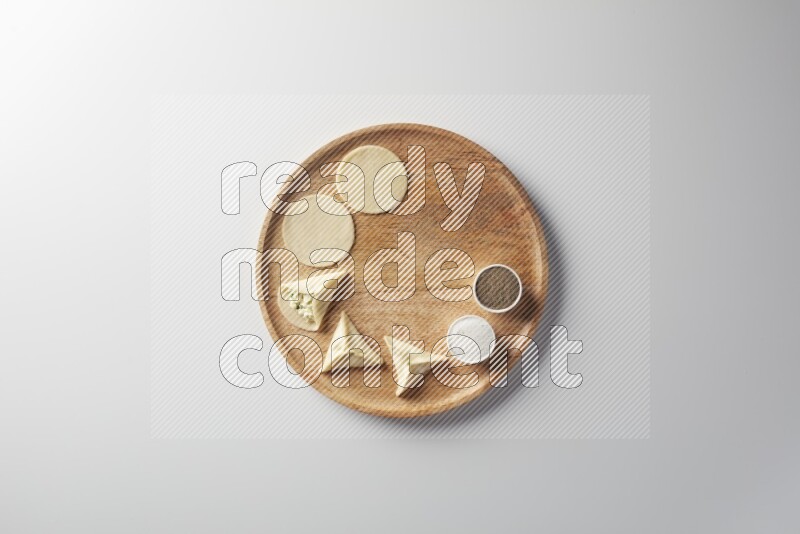 two closed sambosas and one open sambosa filled with cheese while salt, and black pepper aside in a wooden dish on a white background