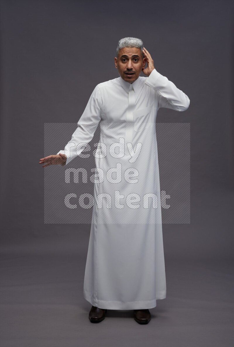 Saudi man wearing thob standing interacting with the camera on gray background