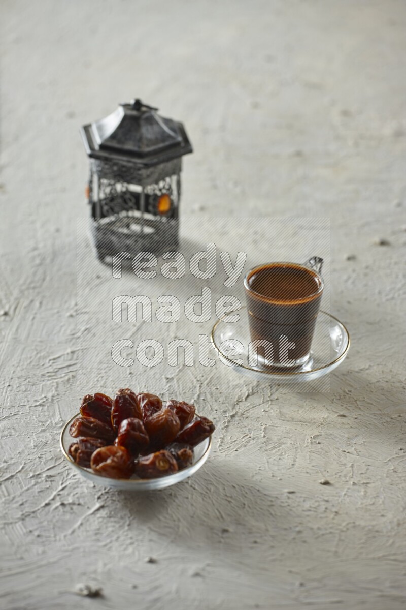 A silver lantern with different drinks, dates, nuts, prayer beads and quran on textured white background