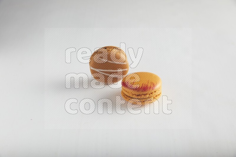 45º Shot of of two assorted Brown Irish Cream, and Orange Exotic macarons on white background