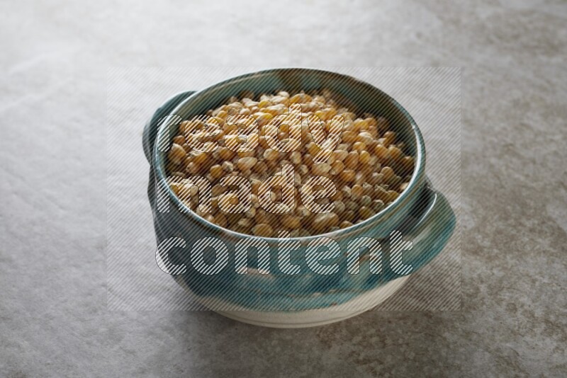 corn kernel in a multi-colored handheld ceramic bowl on a grey textured countertop