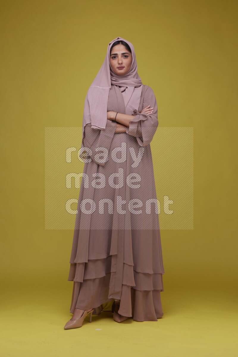 A woman Posing on a Yellow Background wearing Brown Abaya with Hijab