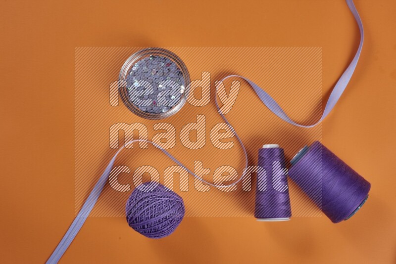 A purple collection of sewing and tailoring tools arranged on a orange background