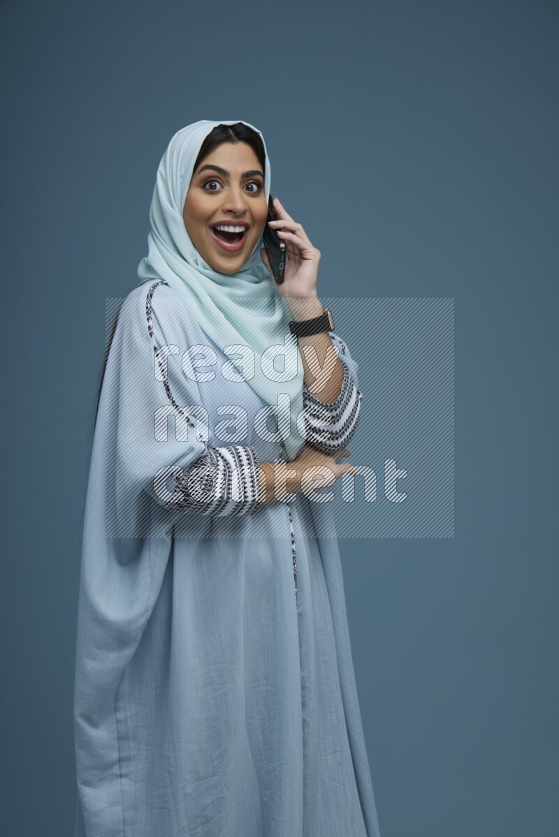A Saudi woman having a Call in a blue background wearing blue Abaya with hijab