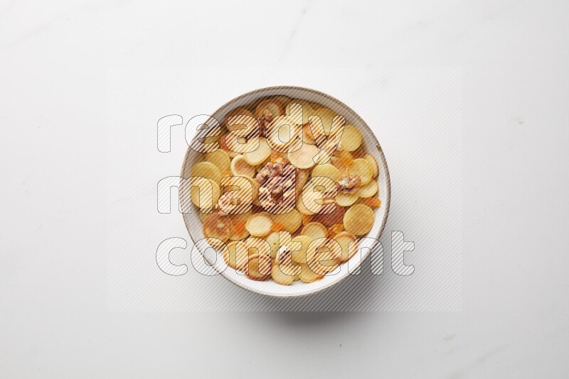 Top-view shot of walnut and apricot cereal pancakes in a round bowl on white background