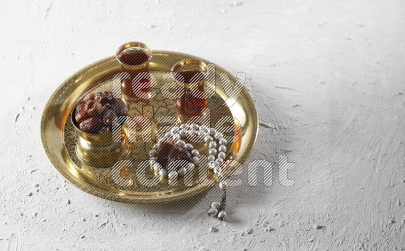 Dates in a metal bowl with tea and prayer beads on a tray in a light setup