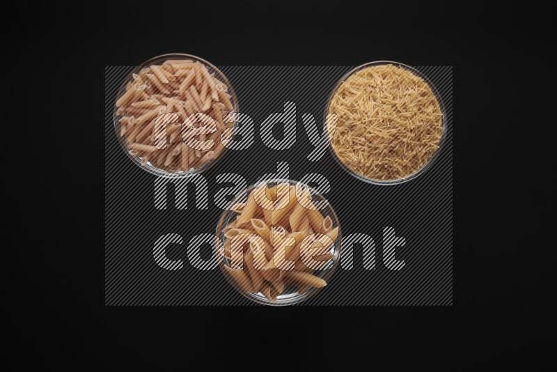 Different pasta types in glass bowls on black background