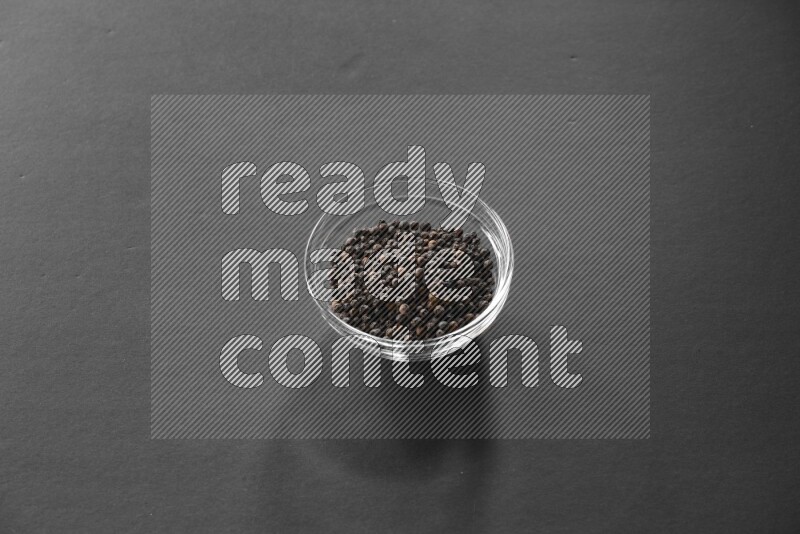 A glass bowl full of black peppers on black flooring