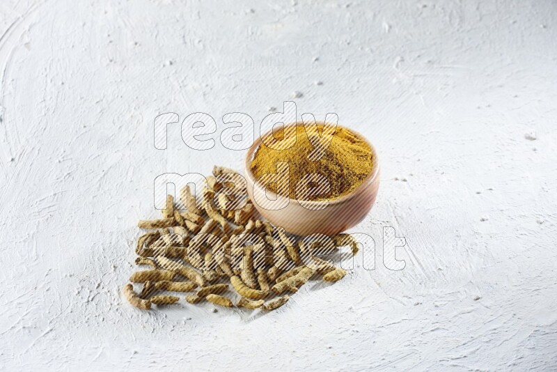 A wooden bowl full of turmeric powder and dried whole fingers beside it on a textured white flooring