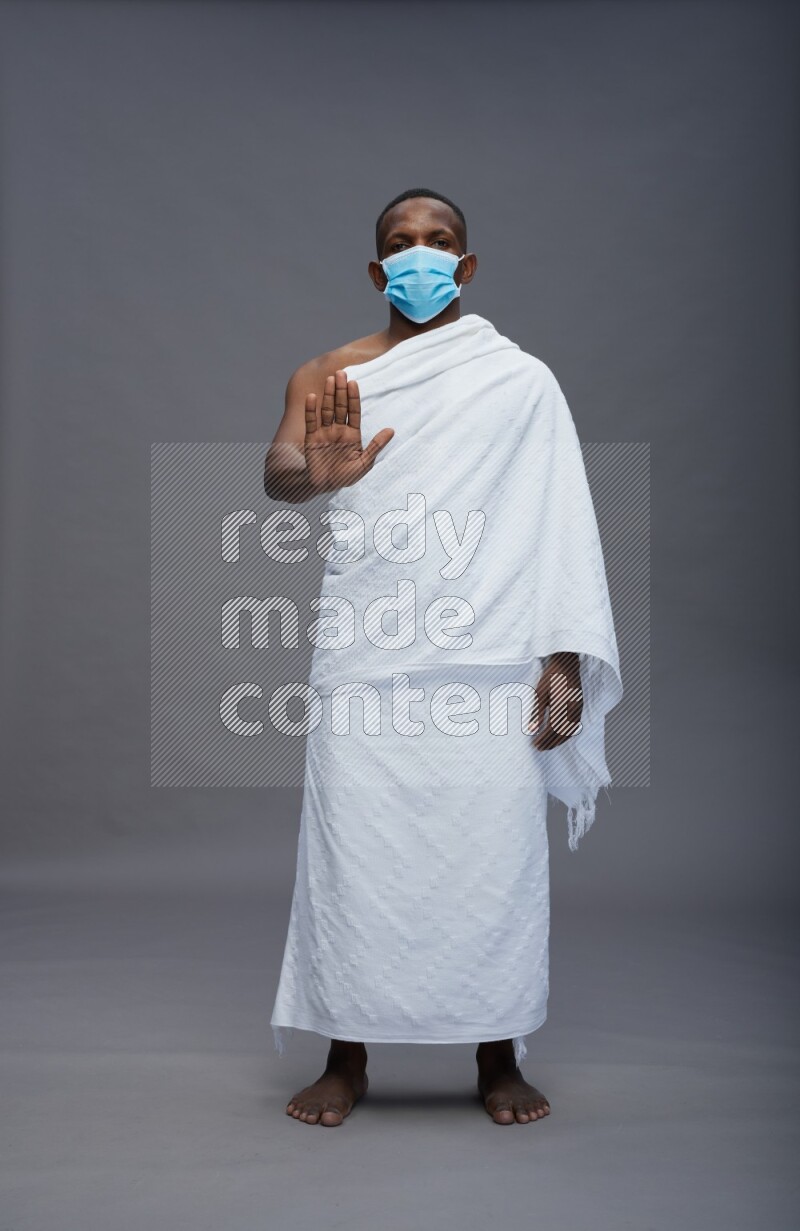 A man wearing Ehram with face mask Standing Interacting with the camera on gray background