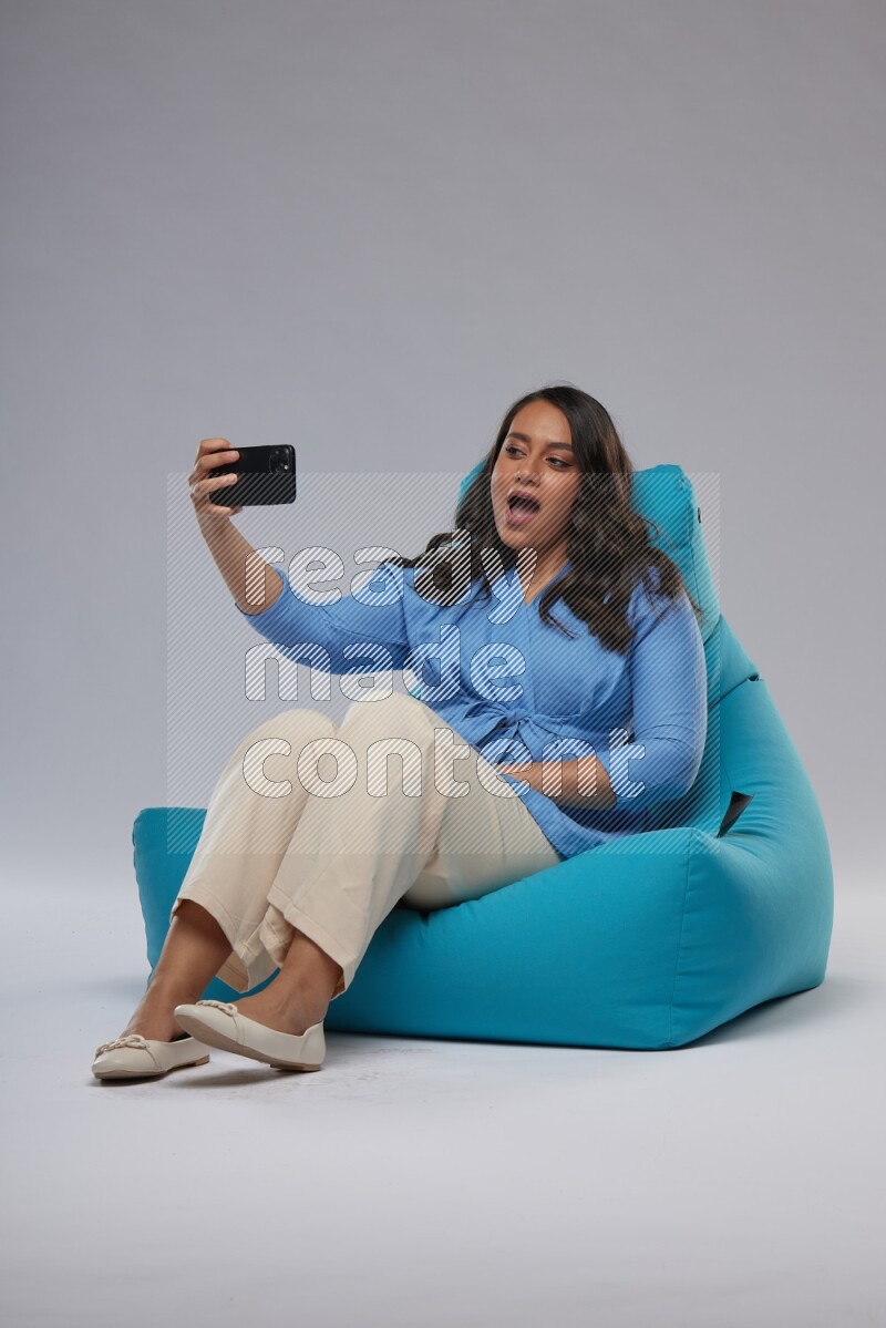 A woman sitting on a blue beanbag and taking selfie