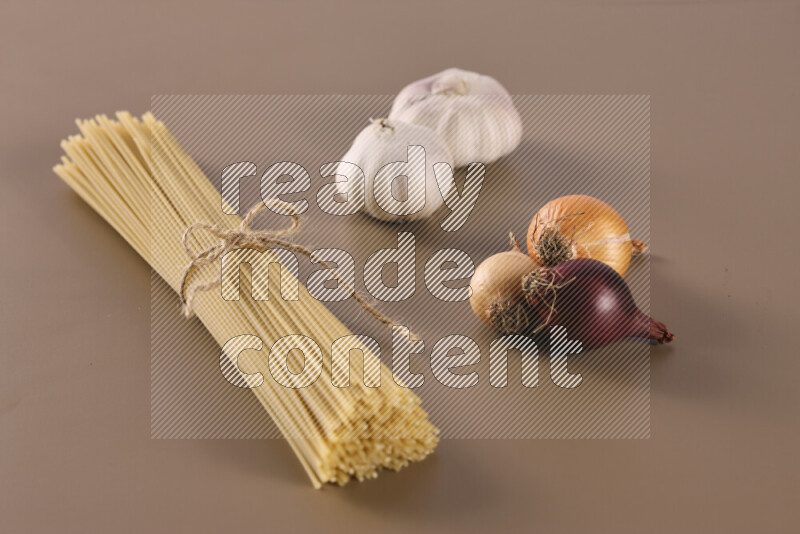 Raw pasta with different ingredients such as cherry tomatoes, garlic, onions, red chilis, black pepper, white pepper, bay laurel leaves, rosemary and cardamom on beige background