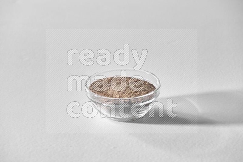 A glass bowl full of black pepper powder on white flooring