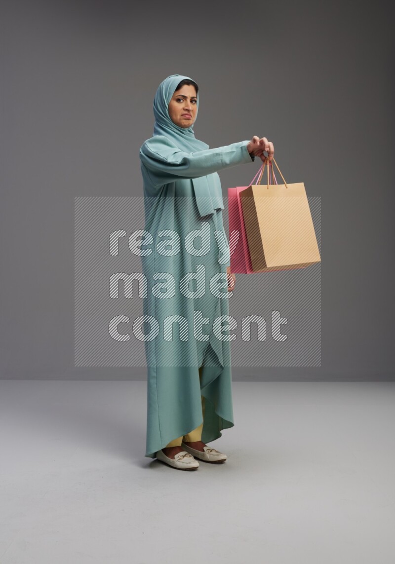 Saudi Woman wearing Abaya standing holding shopping bag on Gray background