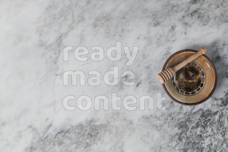 Decorative pottery plate with wooden honey dipper in it on grey marble background