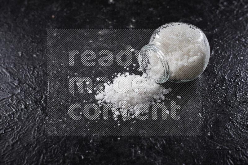 A glass jar full of coarse sea salt crystals on black background