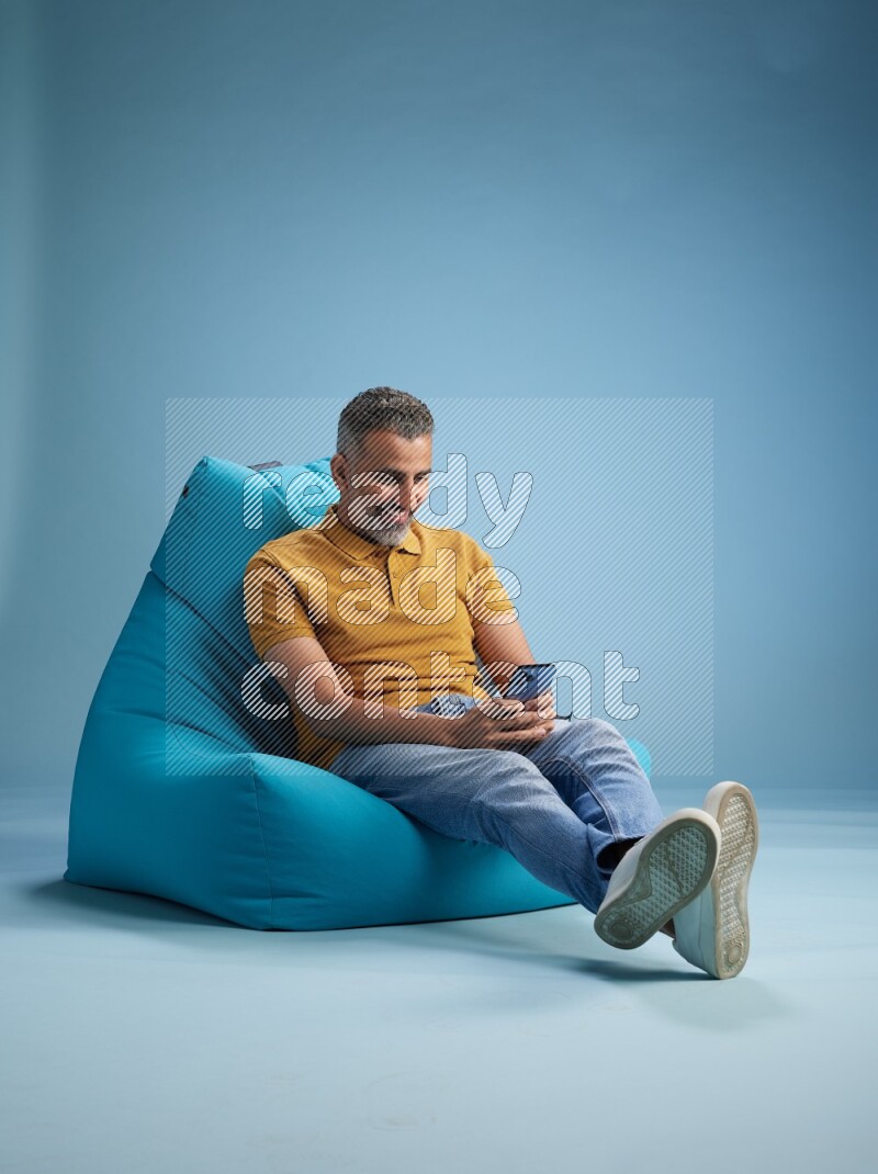 A man sitting on a blue beanbag and texting on phone