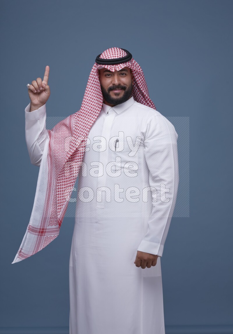 A Saudi man posing on blue background wearing Thob and Shomag