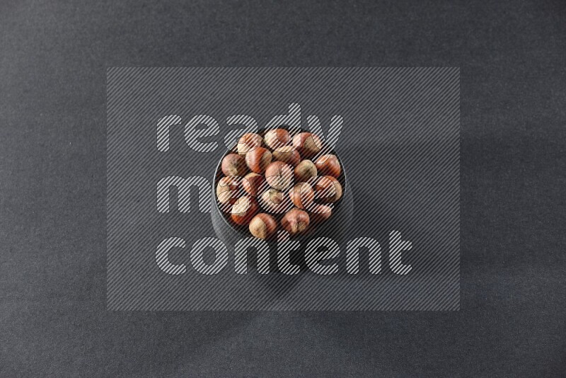 A black pottery bowl full of hazelnuts on a black background in different angles
