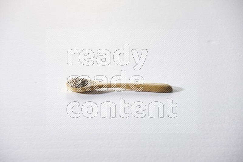 A wooden spoon full of white pepper beads on white flooring