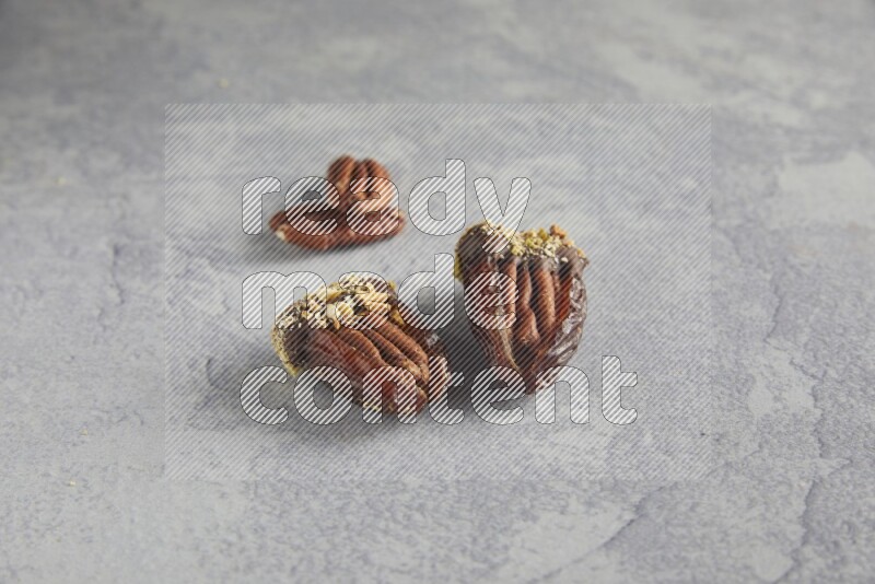 Two pecan stuffed dates covered with Dark chocolate and chopped pistachios on alight grey background