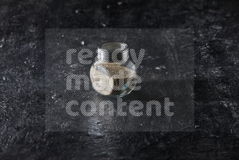 Herbal glass jar full of white pepper on textured black flooring
