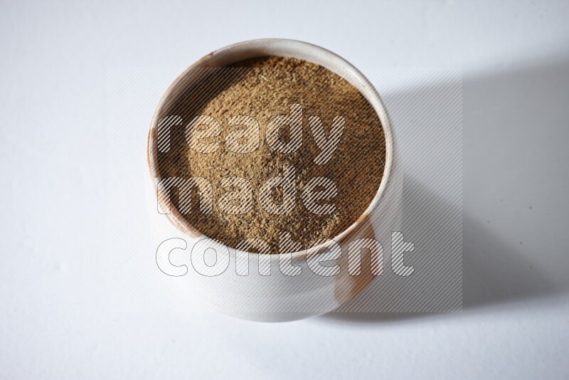 A beige bowl full of cumin powder on a white flooring