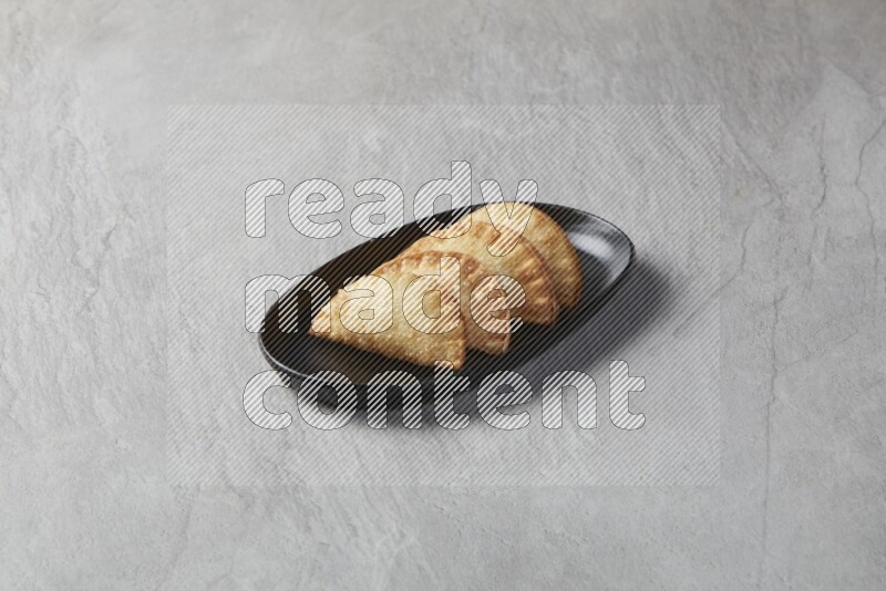Four fried sambosas in an oval shaped black plate on a gray background