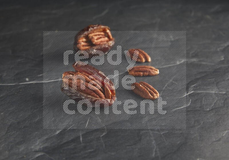 two pecan stuffed madjoul dates on a black textured background