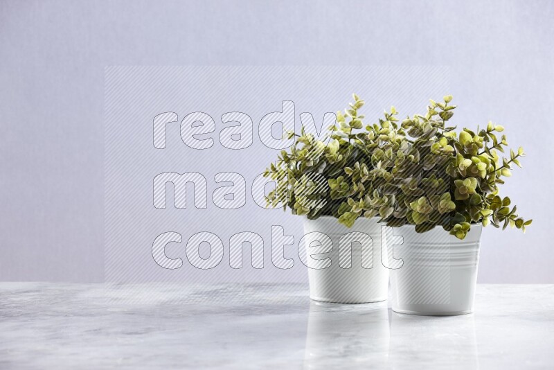 Two green artificial plants in white pot on grey marble background