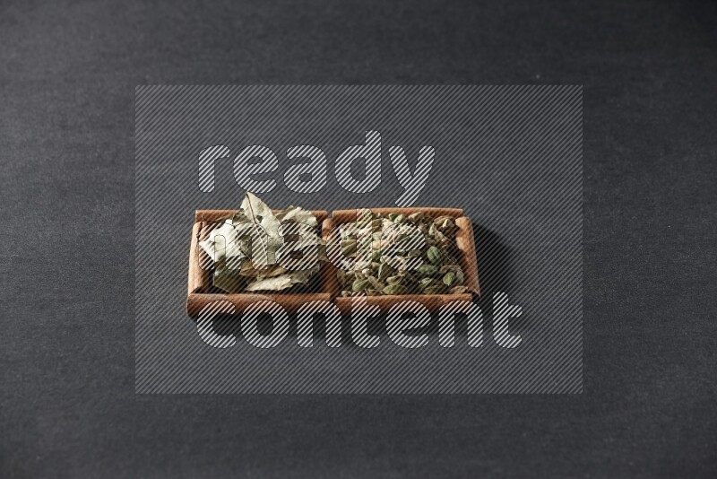 مربعان من أعواد القرفة ممتلئان بحبوب الهيل وأوراق الغار علي خلفية سوداء