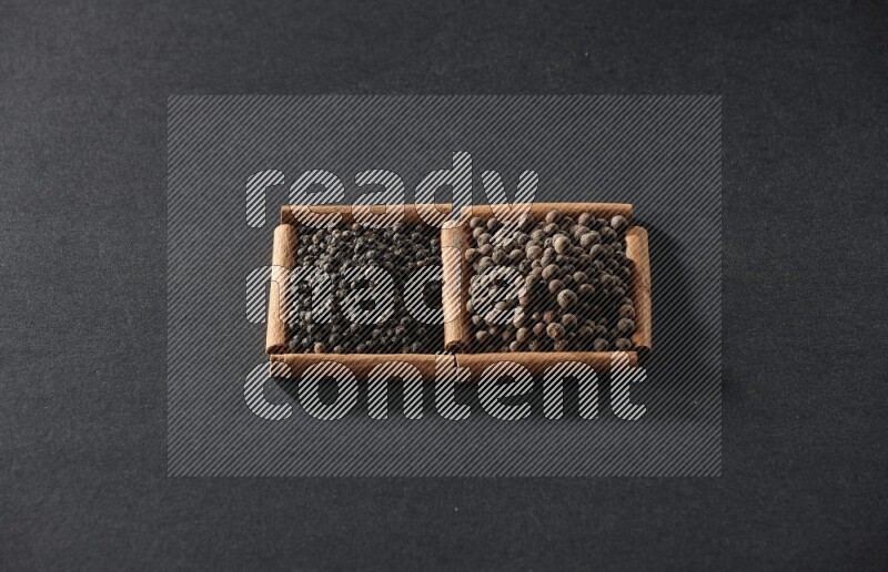 2 squares of cinnamon sticks full of black peppers and allspice on black flooring