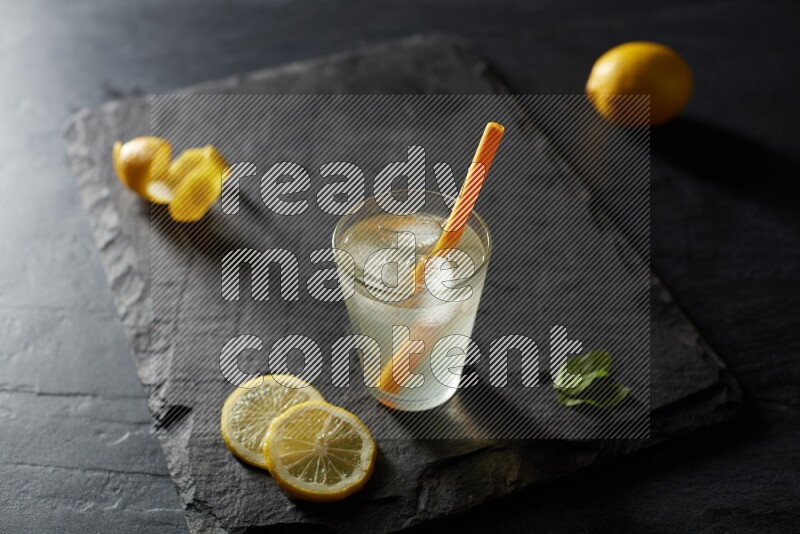 A glass of lemon juice with a straw on black background