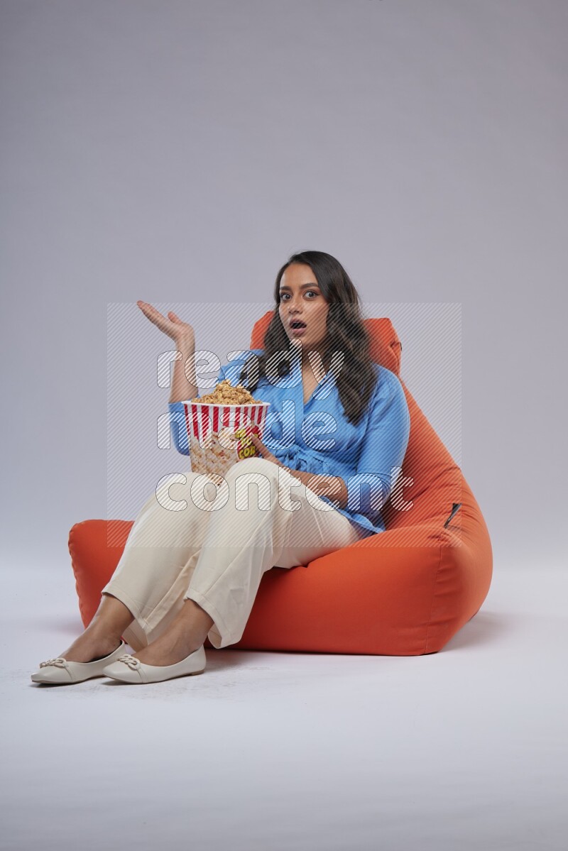 A woman sitting on an orange beanbag and eating popcorn