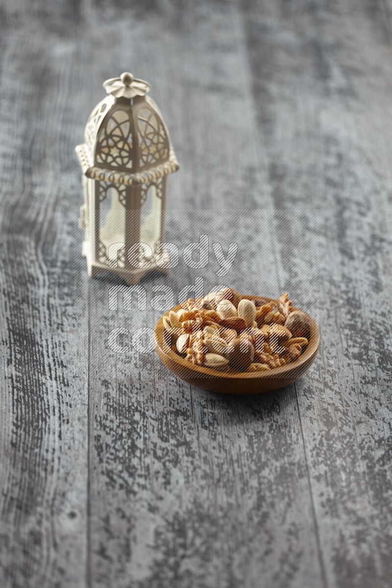 A white lantern with different drinks, dates, nuts, prayer beads and quran on grey wooden background
