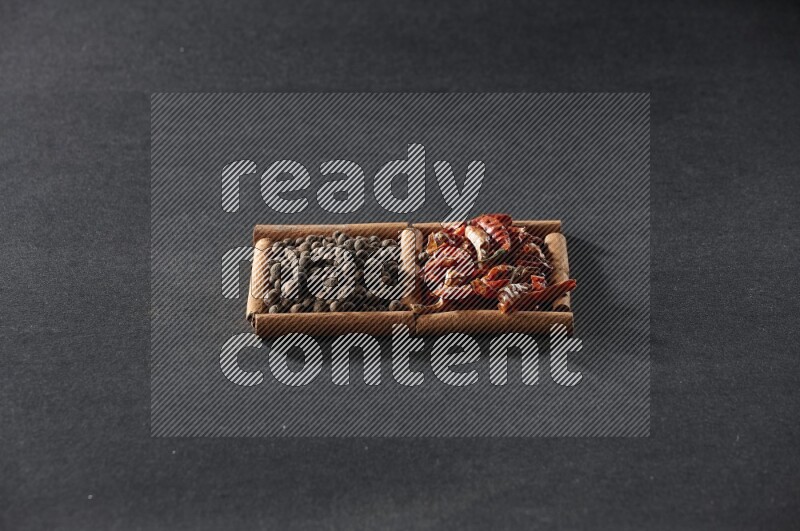 مربعان من أعواد القرفة ممتلئان بالفلفل الحار المجفف وحبوب بهار الفلفل الحلو علي خلفية سوداء