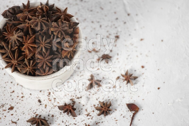Star Anise in a white bowl and more of it sprinkled on white background