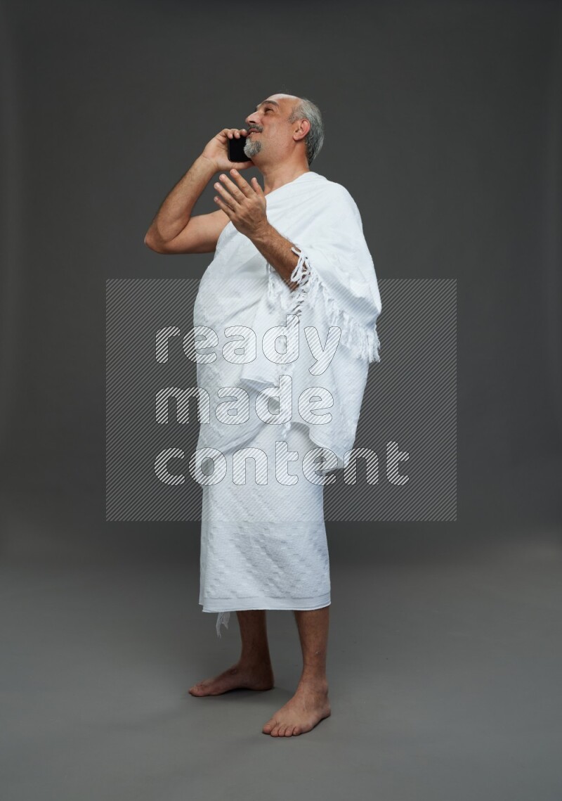 A man wearing Ehram Standing talking on phone on gray background