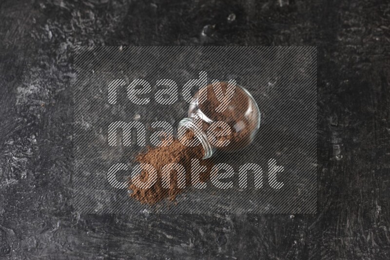 وعاء زجاجي للتوابل مقلوب ممتلئ ببودرة القرنفل والبودرة سقطت منه على أرضية سوداء