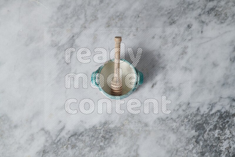 Multicolored pottery bowl with wooden honey dipper in it on grey marble background