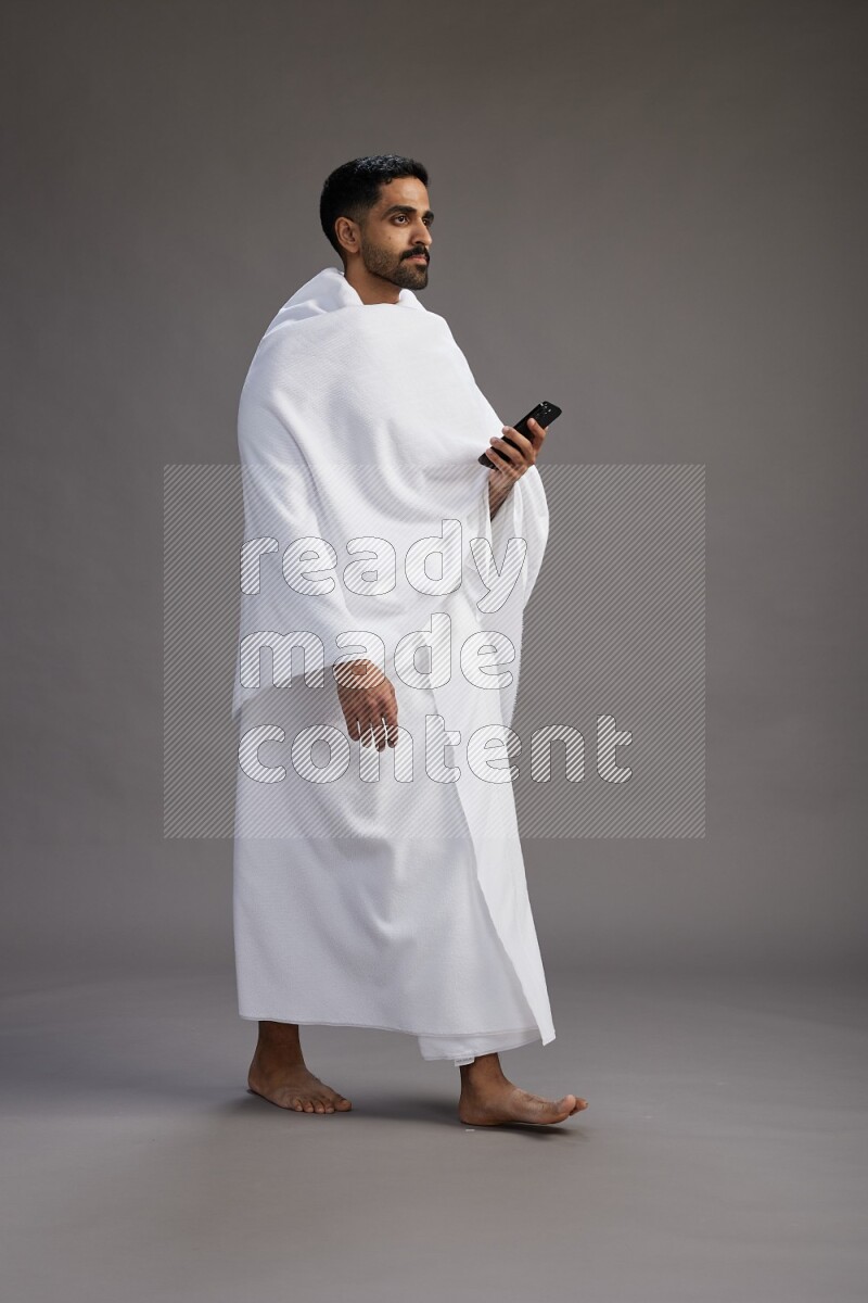 A man wearing Ehram Standing texting on phone on gray background