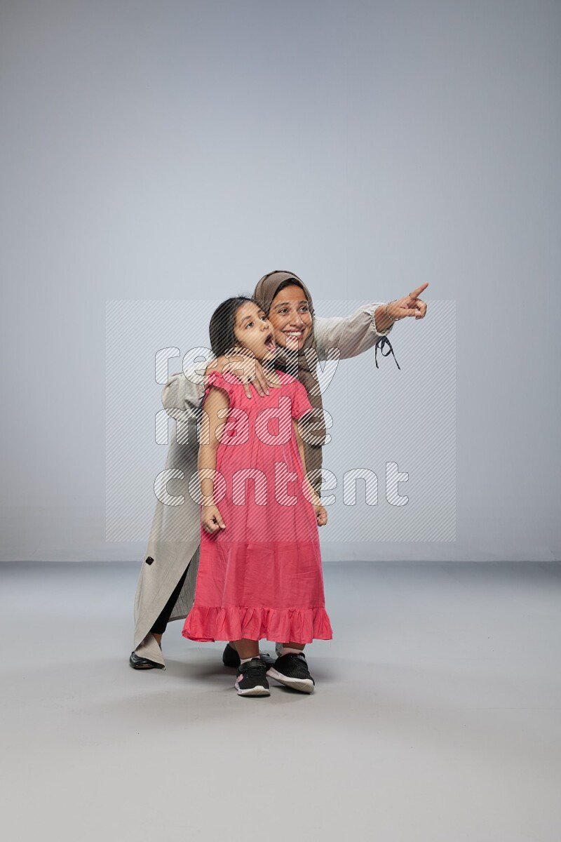 A girl and her mother interacting with the camera on gray background