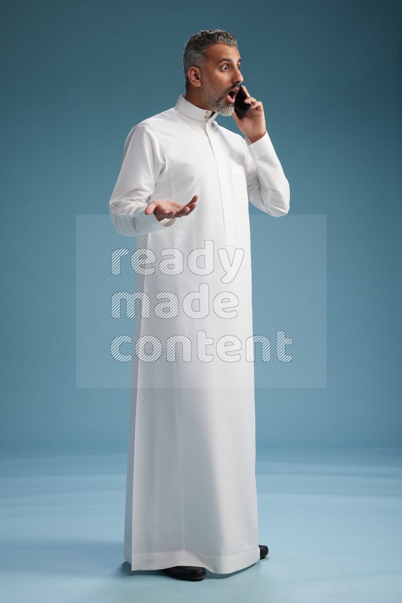 Saudi man wearing thob talking on the phone on blue background