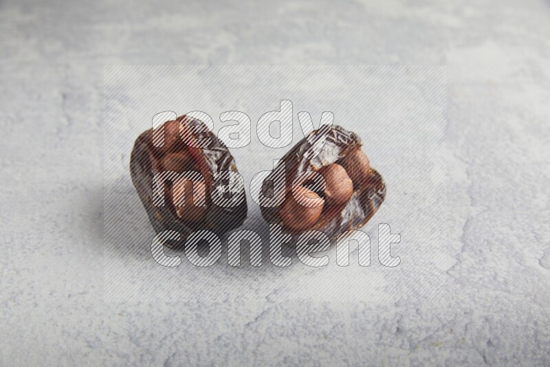 two hazelnuts stuffed madjoul dates on a light grey background