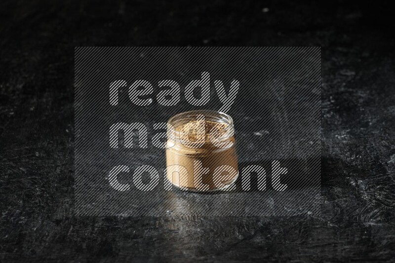 وعاء زجاجي ممتلئ ببودرة بهار الفلفل الحلو على خلفية سوداء