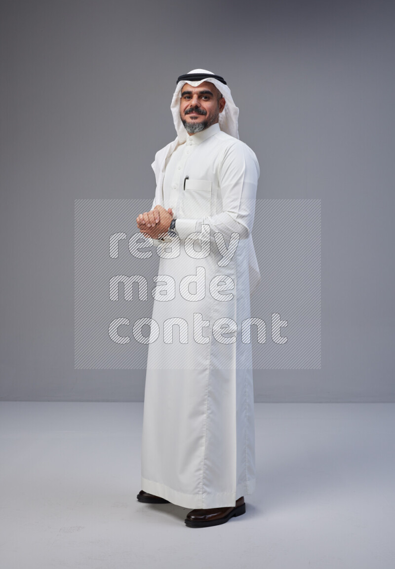 Saudi man Wearing Thob and white Shomag standing interacting with the camera on Gray background
