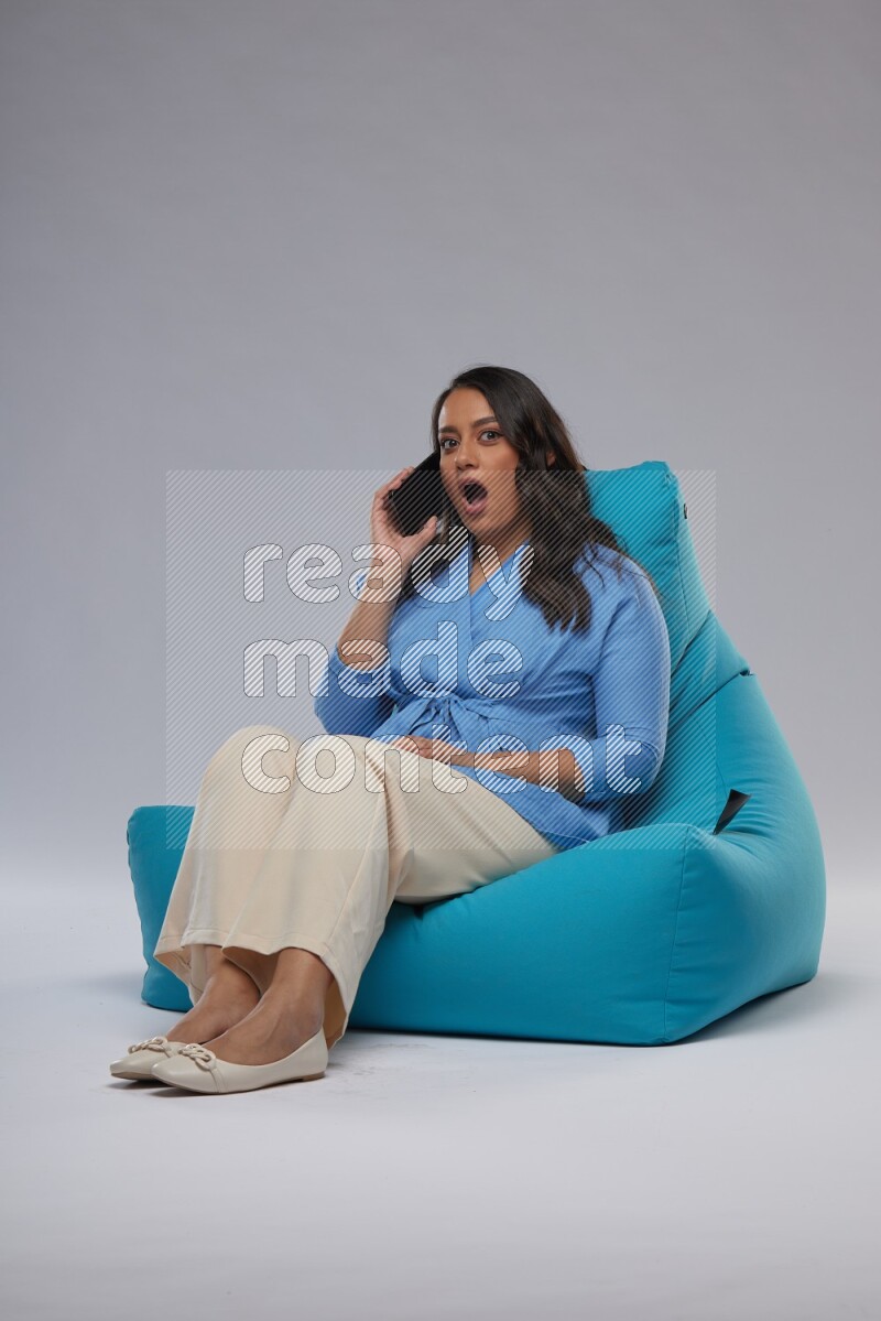 A woman sitting on a blue beanbag and talking on the phone
